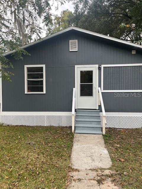 The exterior of a gray house features a white front door, stairs, and lattice skirting — 25317 NW 6TH AVENUE, NEWBERRY, FL