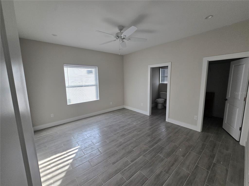 An empty bedroom features light gray walls, wood-look tile flooring, a ceiling fan, and two doorways — 29469 PEACE RIVER SHORES BOULEVARD, PUNTA GORDA, FL