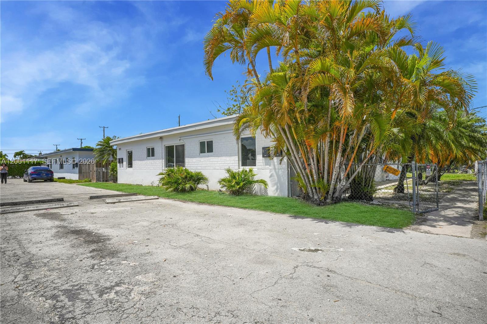A white, single-story building with a palm tree stands next to a paved parking lot — 11775 SW 223rd St, Miami FL 33170, MIAMI, FL