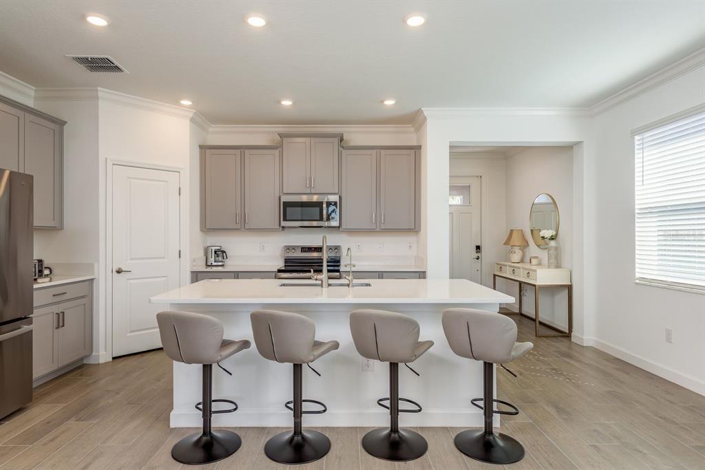 A kitchen features gray cabinets, a white island with four stools, and light wood flooring — 10661 TUPPER CAY DRIVE, SAN ANTONIO, FL