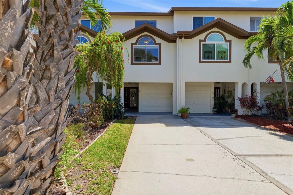 The exterior of a multi-story townhouse complex features white stucco walls, arched windows, and garages — 381 MADEIRA CIRCLE, TIERRA VERDE, FL