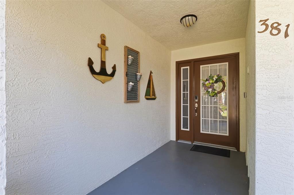 A covered entryway features a brown front door with a wreath and nautical wall decor — 381 MADEIRA CIRCLE, TIERRA VERDE, FL