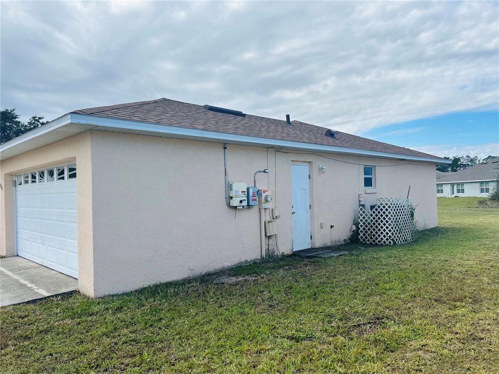 The exterior side of a house features a garage, a door, and utility equipment — 1731 MINNOW COURT, POINCIANA, FL