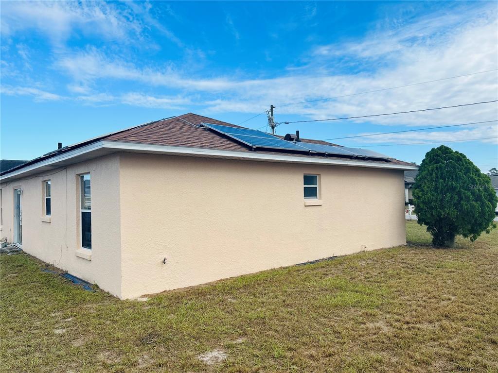 A side view of a beige house with solar panels on the shingled roof — 1731 MINNOW COURT, POINCIANA, FL