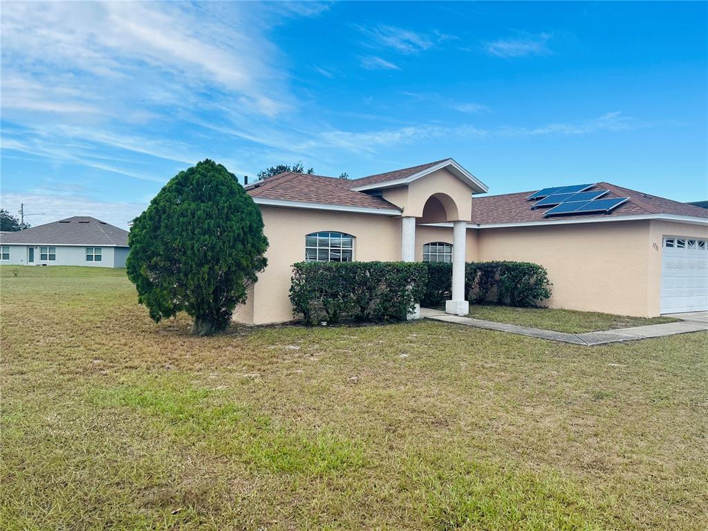 A single-story peach-colored house with a brown shingled roof, solar panels, and a large tree — 1731 MINNOW COURT, POINCIANA, FL