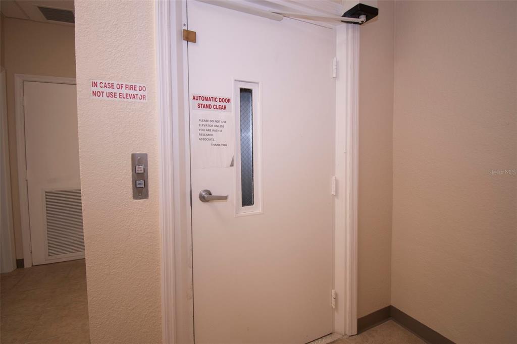 A white door with signage and an elevator call button in a plain hallway — 3221 TAMIAMI TRL UNIT 16, PORT CHARLOTTE, FL