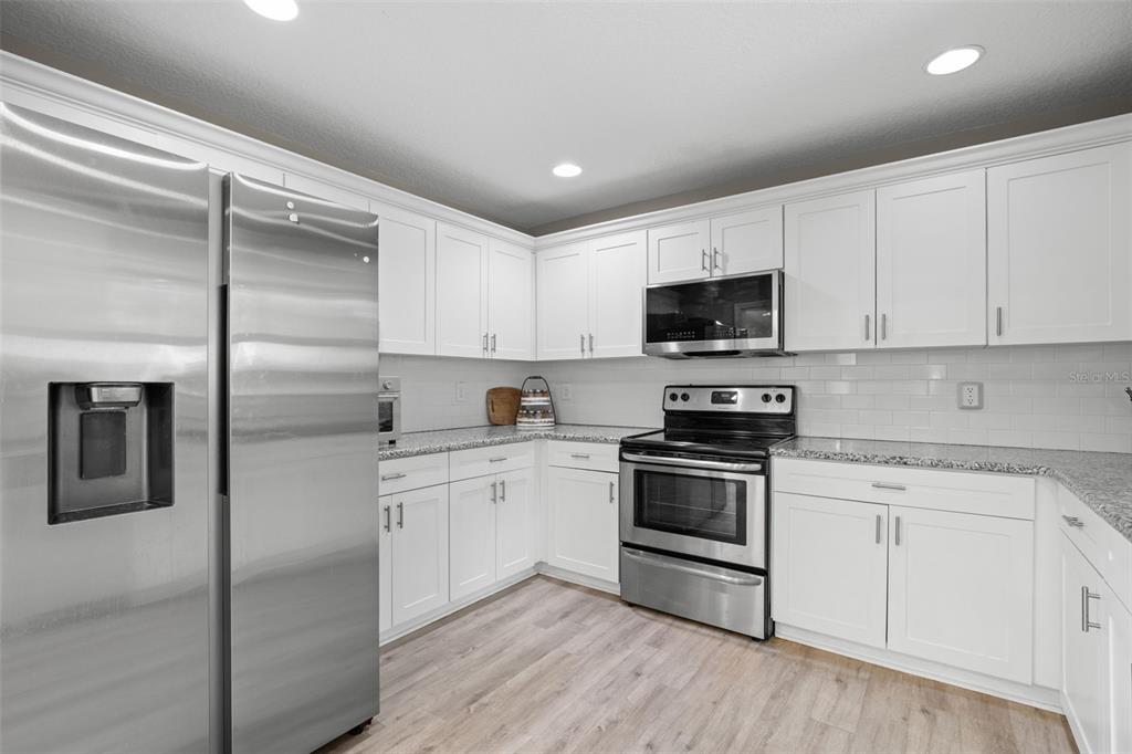 A modern kitchen features white cabinets, stainless steel appliances, and speckled granite countertops — 3822 W EUCLID AVENUE, TAMPA, FL