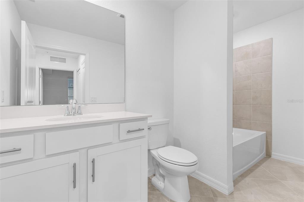 A modern bathroom features a white vanity, a toilet, and a tiled bathtub shower combination — 14191 HERITAGE LANDING BOULEVARD UNIT 1214, PUNTA GORDA, FL