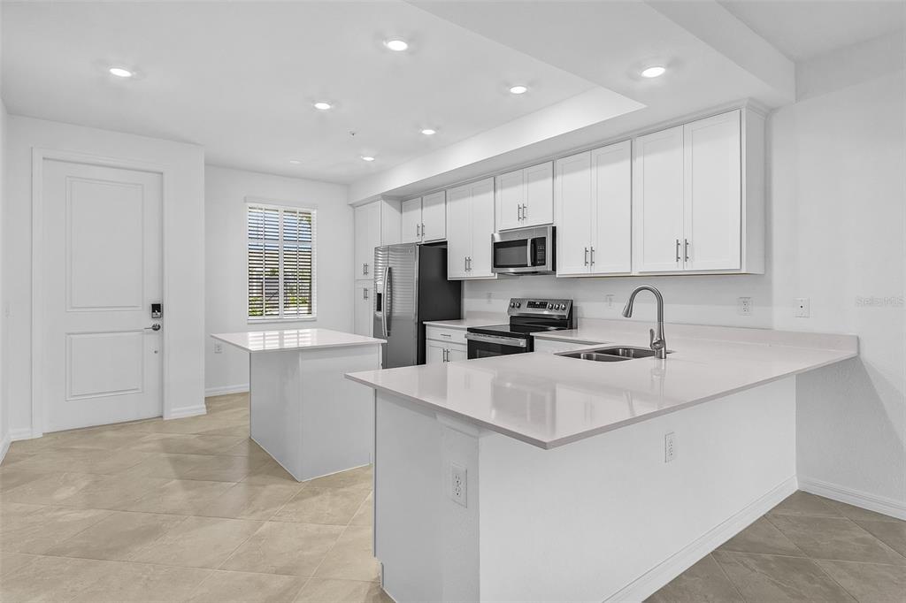 A modern kitchen features white cabinetry, stainless steel appliances, a center island, and tile flooring — 14191 HERITAGE LANDING BOULEVARD UNIT 1214, PUNTA GORDA, FL