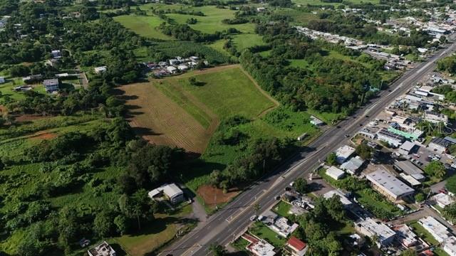 An aerial view shows a large, undeveloped grassy lot adjacent to a paved highway — PR 2 KM. 120.6, AGUADILLA, PR