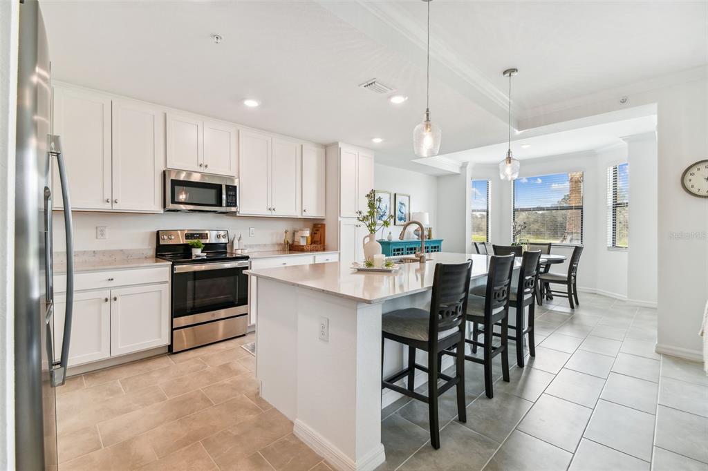 A modern kitchen features white cabinetry, stainless steel appliances, a large island, and tile flooring — 18114 GAWTHROP DRIVE UNIT 106, BRADENTON, FL
