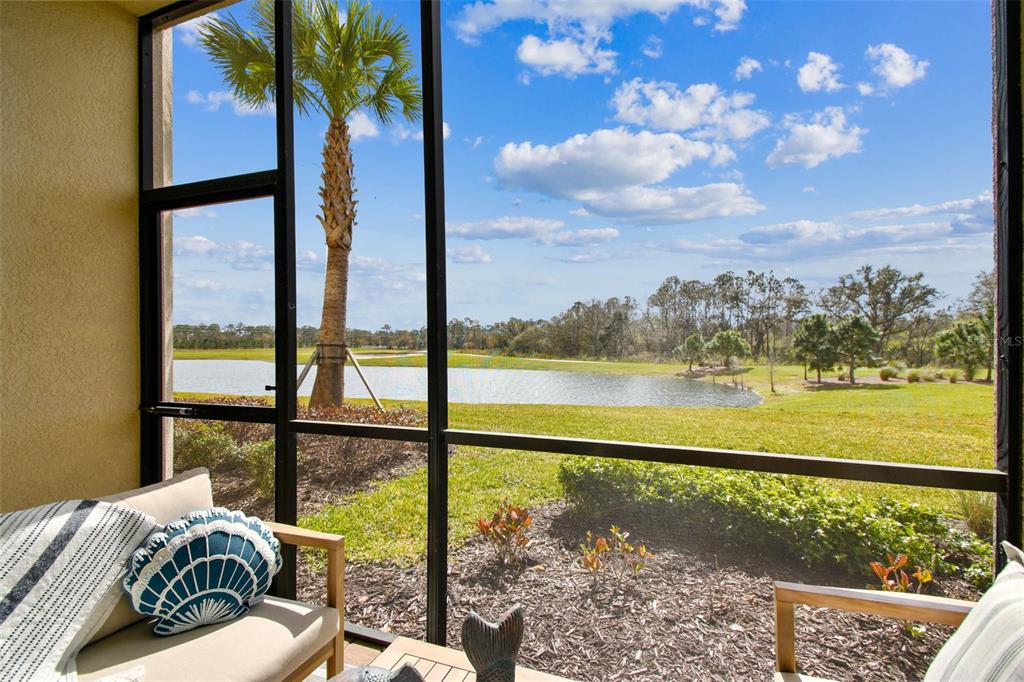 A screened-in patio overlooks a grassy lawn, a small pond, and a palm tree — 18114 GAWTHROP DRIVE UNIT 106, BRADENTON, FL