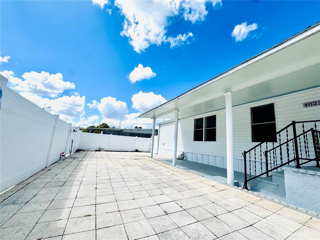 A paved patio area sits beside a white house with a covered porch and railing — 4822 ROLLING MEADOW DRIVE, LAKELAND, FL