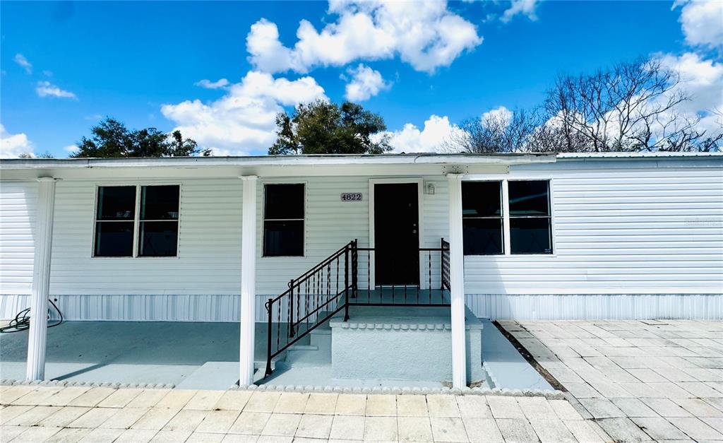 A white mobile home features a covered porch, black railings, and a paved front area — 4822 ROLLING MEADOW DRIVE, LAKELAND, FL