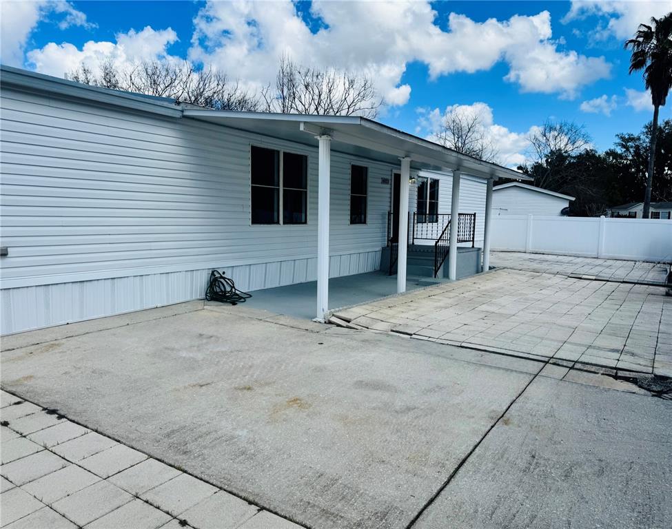 A white mobile home features a covered porch, concrete driveway, and a paved patio area — 4822 ROLLING MEADOW DRIVE, LAKELAND, FL