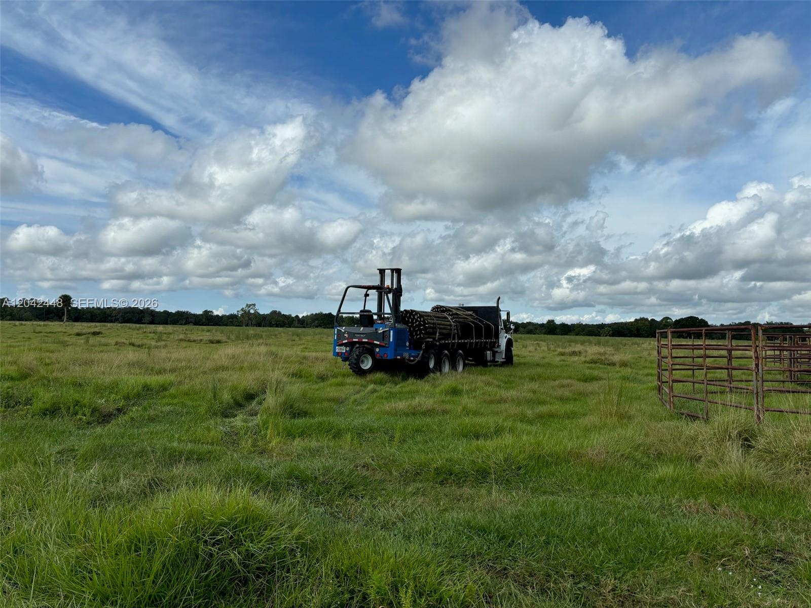 A truck carrying a load of wooden poles sits in a grassy field — 25952 SW Jockeys Run, Stuart FL 34974, STUART, FL