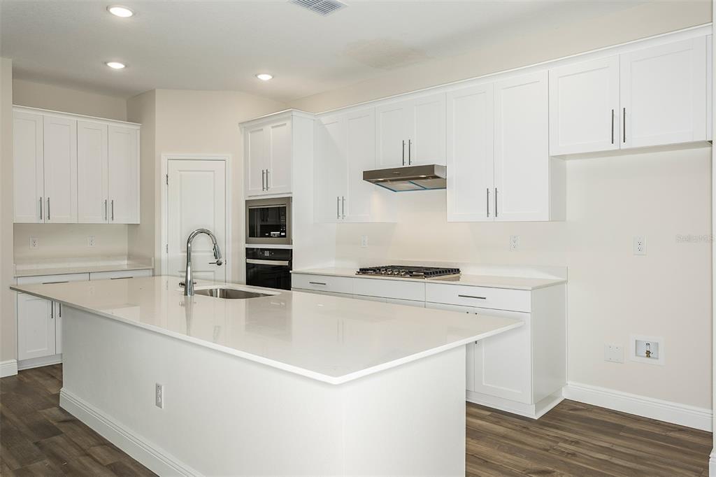 A modern kitchen features white cabinets, quartz countertops, a large island, and stainless steel appliances — 33580 HAMMOCK BEACH WAY, DADE CITY, FL