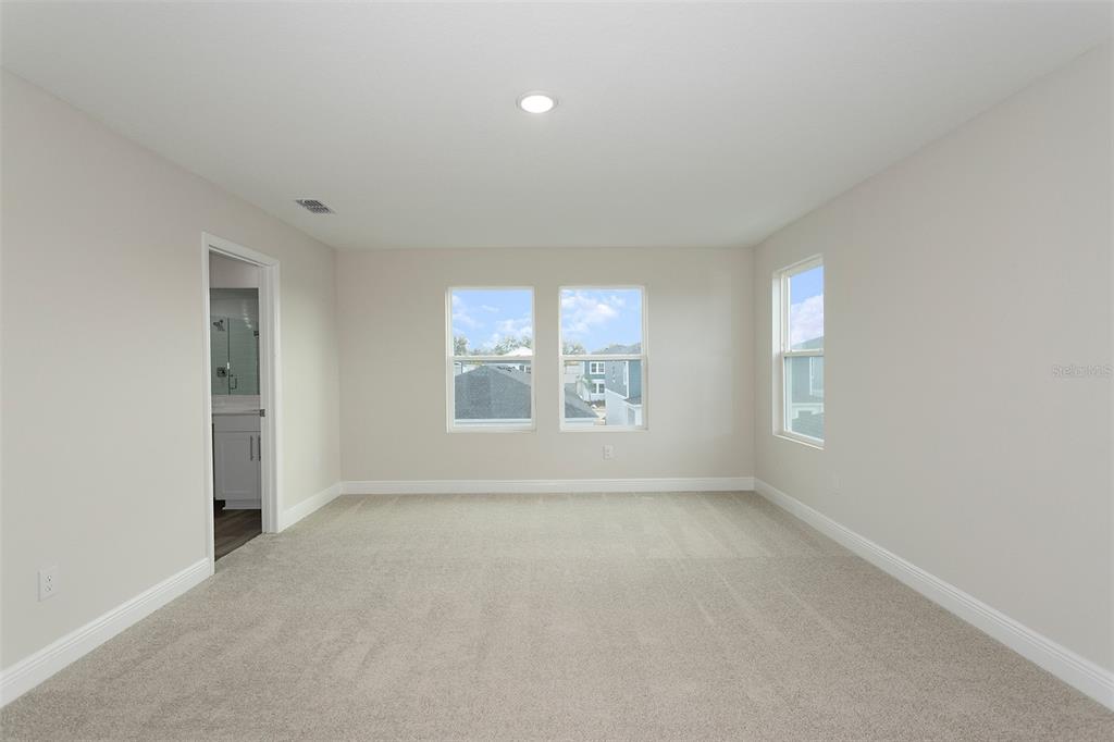 A carpeted bedroom with neutral walls, three windows, and a doorway leading to a bathroom — 33580 HAMMOCK BEACH WAY, DADE CITY, FL