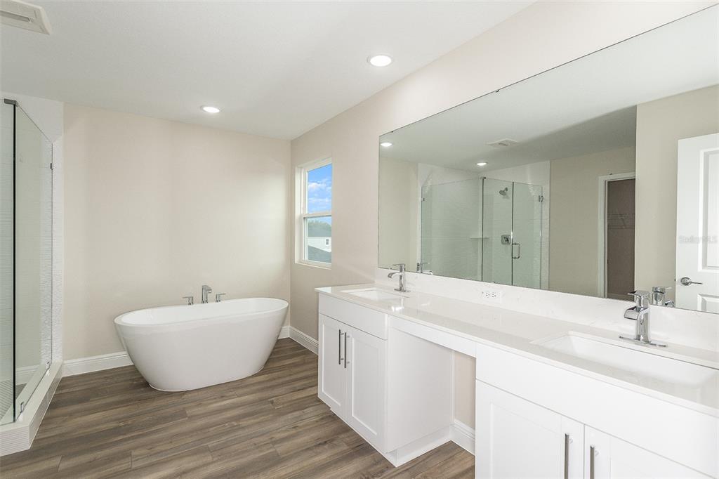 A modern bathroom features a freestanding tub, a double vanity with white cabinets, and wood-look flooring — 33580 HAMMOCK BEACH WAY, DADE CITY, FL