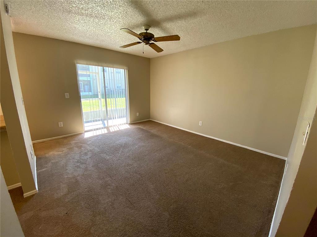 An empty room features beige carpet, tan walls, a ceiling fan, and a sliding glass door — 4148 PERSHING POINTE PLACE UNIT 1, ORLANDO, FL