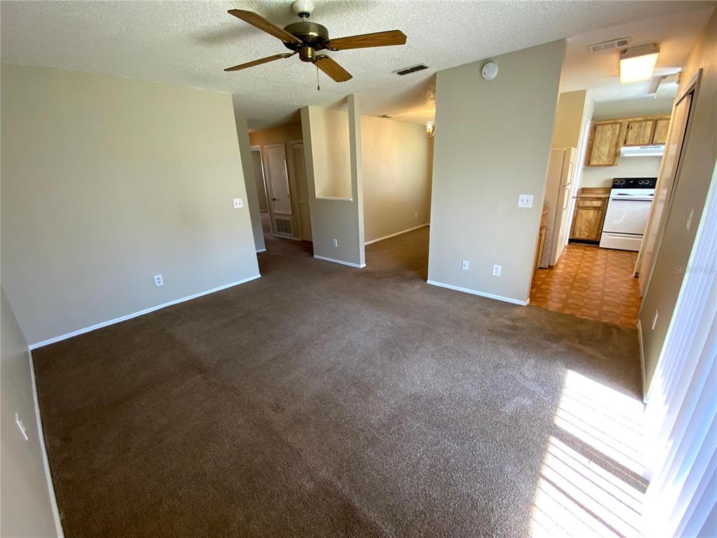 An interior view shows a carpeted living area leading to a kitchen with wood cabinets — 4148 PERSHING POINTE PLACE UNIT 1, ORLANDO, FL