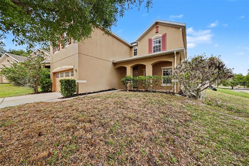 A two-story tan stucco house with a covered front porch and a two-car garage — 30030 MESSARA COVE, MOUNT DORA, FL