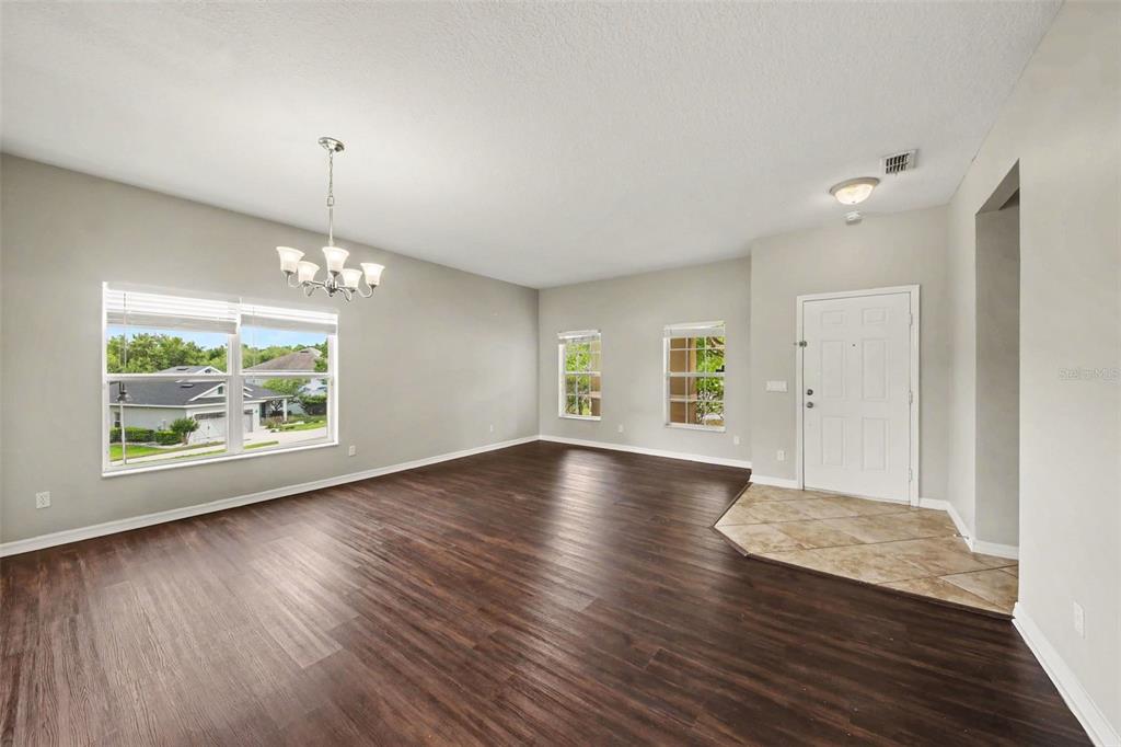 An empty living room with dark wood flooring, a chandelier, and a tiled entryway — 30030 MESSARA COVE, MOUNT DORA, FL