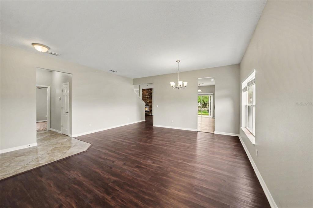 An open living area features dark wood-look flooring, light gray walls, and a chandelier — 30030 MESSARA COVE, MOUNT DORA, FL