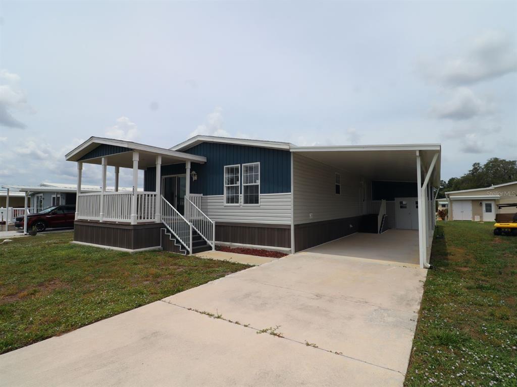 A single-story manufactured home with a front porch, carport, and concrete driveway — 204 EL PRADO, NORTH PORT, FL