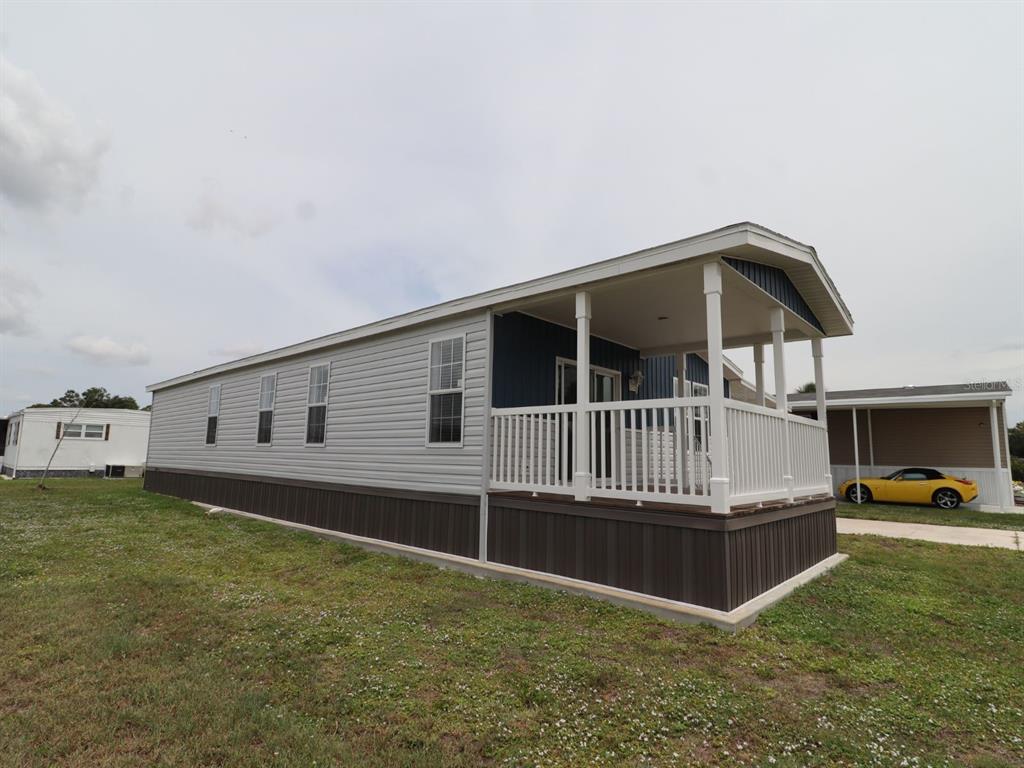A manufactured home with light gray siding, a dark brown base, and a covered front porch — 204 EL PRADO, NORTH PORT, FL