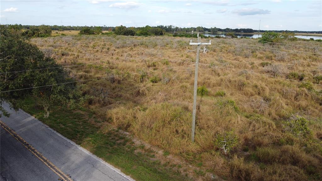An aerial view shows a paved road running alongside a large, undeveloped grassy field — 7630 LAKE BUFFUM ROAD N, FORT MEADE, FL