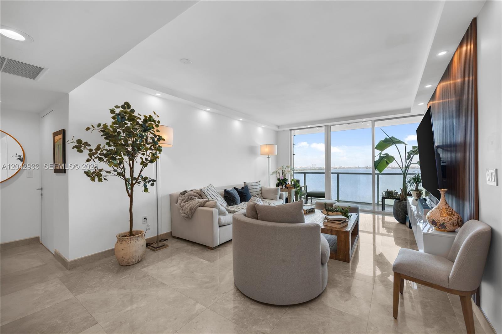 A modern living room features marble floors, a sofa, accent chairs, and a waterfront balcony — 665 NE 25th St # 1503, Miami FL 33137, MIAMI, FL