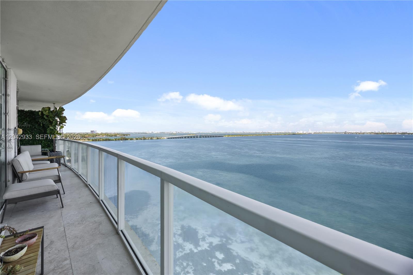A high-rise balcony features outdoor seating, a glass railing, and a panoramic water view — 665 NE 25th St # 1503, Miami FL 33137, MIAMI, FL