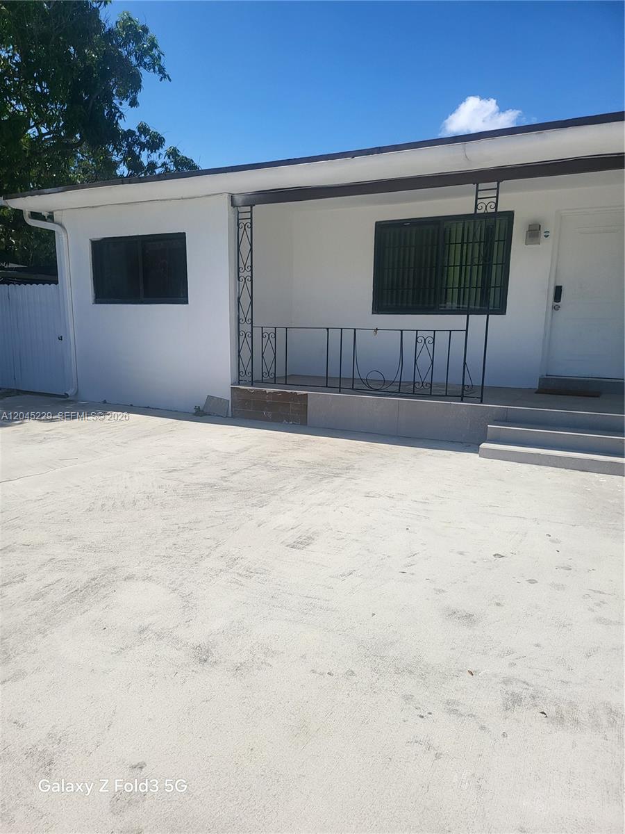 The exterior of a white house features a concrete driveway, a small porch, and metal railings — 2467 NW 95th Ter, Miami FL 33147, MIAMI, FL