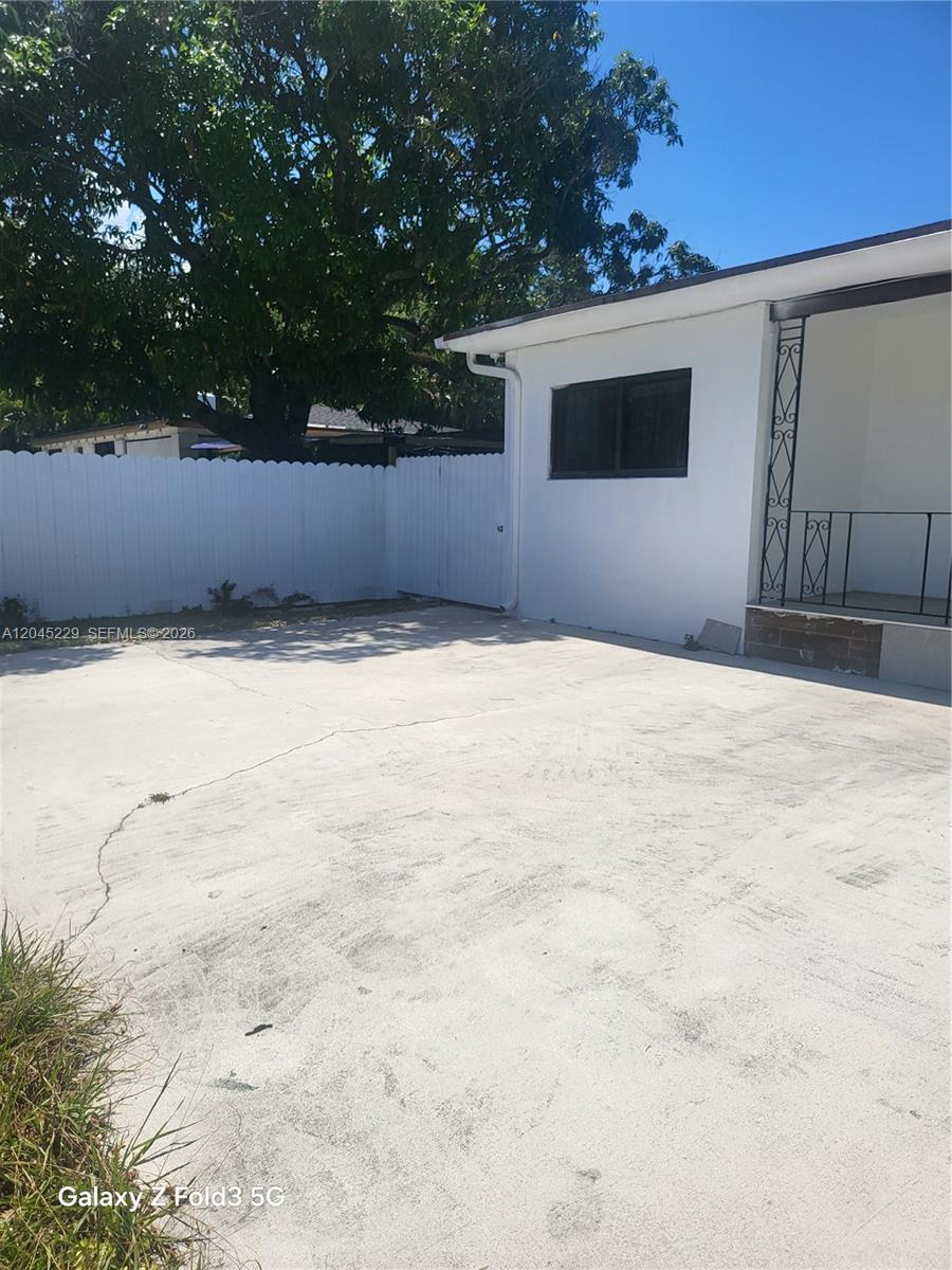 A concrete driveway leads to a white house with a covered porch and fenced yard — 2467 NW 95th Ter, Miami FL 33147, MIAMI, FL