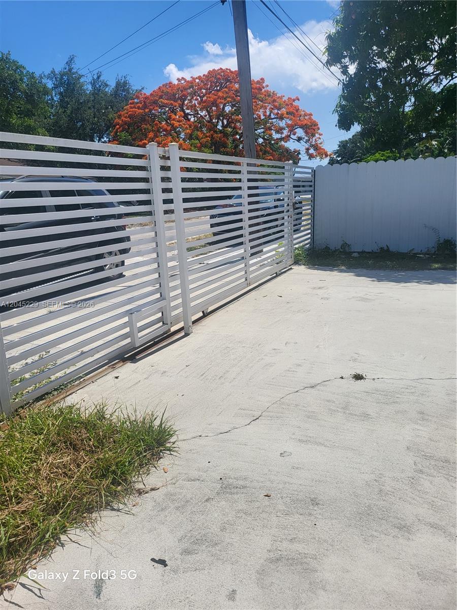A white horizontal slat metal gate stands on a concrete driveway next to a fence — 2467 NW 95th Ter, Miami FL 33147, MIAMI, FL
