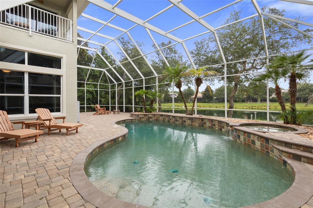 A screened-in patio features a swimming pool, a hot tub, and lounge chairs overlooking water — 10 N VILLAGE PARKWAY, PALM COAST, FL