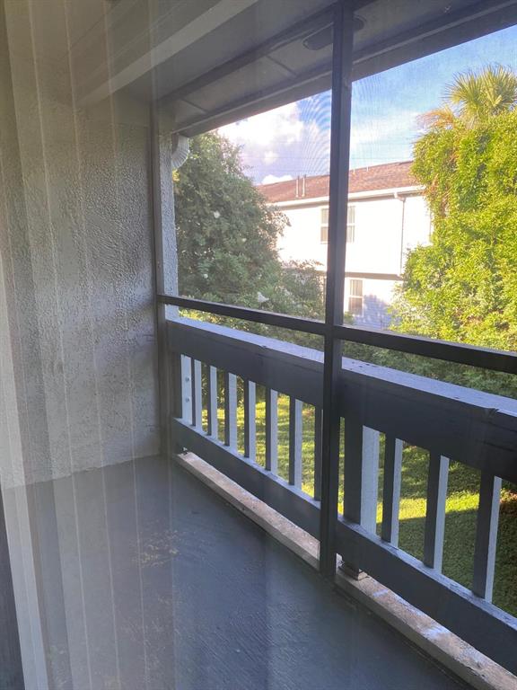 A screened-in balcony features a gray floor, wooden railings, and a view of trees — 4749 S TEXAS AVENUE UNIT 4749C, ORLANDO, FL