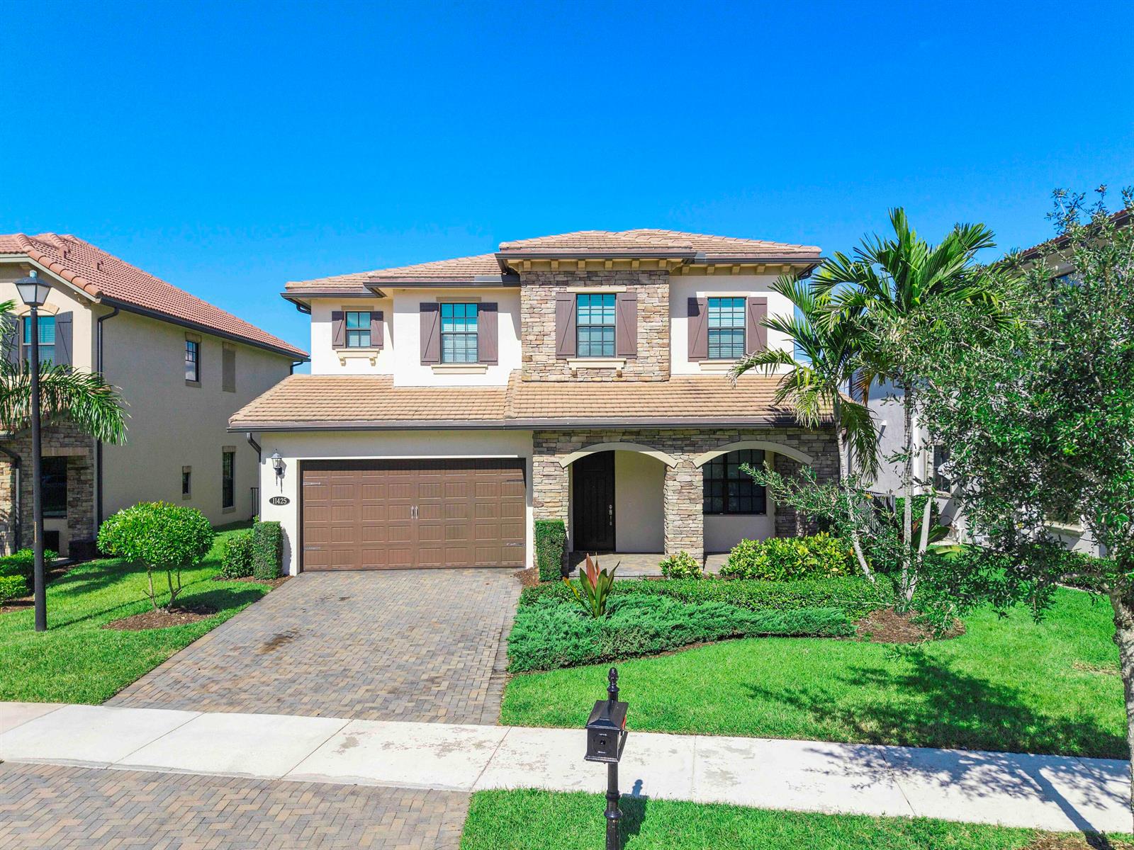 A two-story suburban house with a stone facade, brown garage door, and a paved driveway — 11425 Watercrest Circle E, Parkland FL 33076, PARKLAND, FL