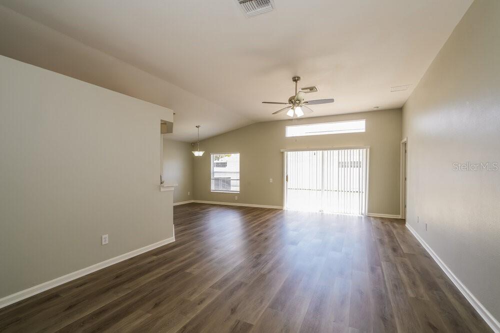 An empty living room features light-colored walls, wood-look flooring, a ceiling fan, and sliding doors — 12534 HERONS PATH PLACE, RIVERVIEW, FL