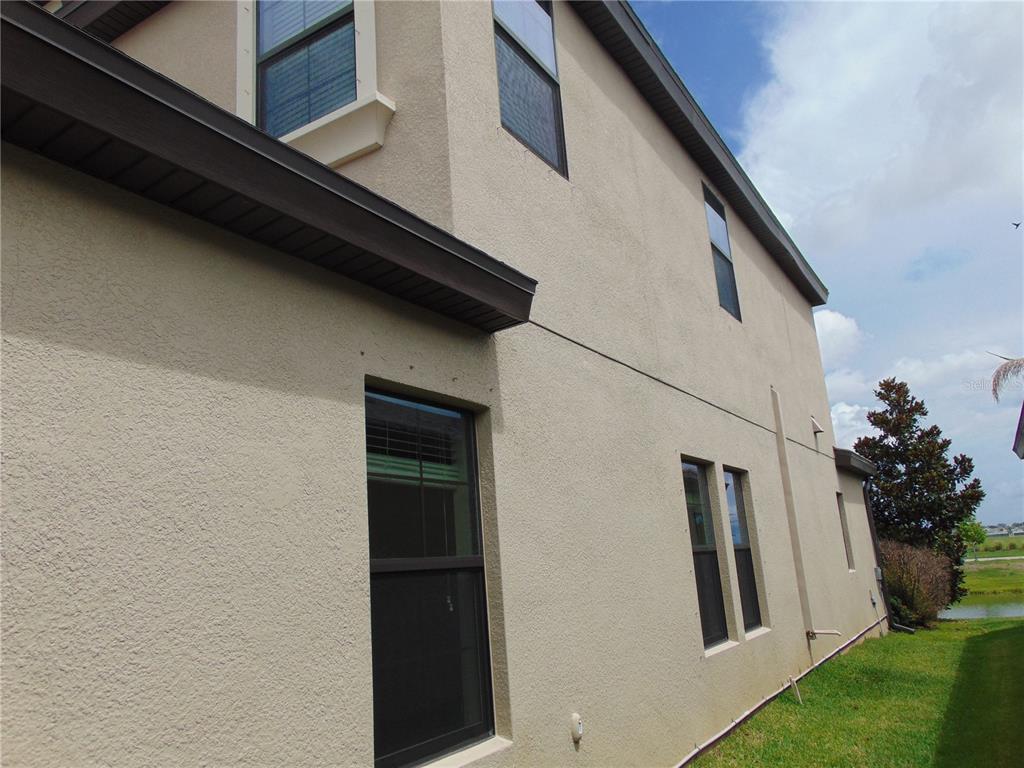 The exterior side view of a two-story beige stucco house with dark-framed windows — 13107 MONACH ISLES DRIVE, RIVERVIEW, FL