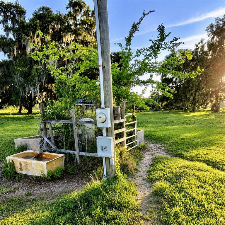 A utility pole with an electrical meter stands in a grassy field near livestock troughs — MONDON HILL ROAD, BROOKSVILLE, FL