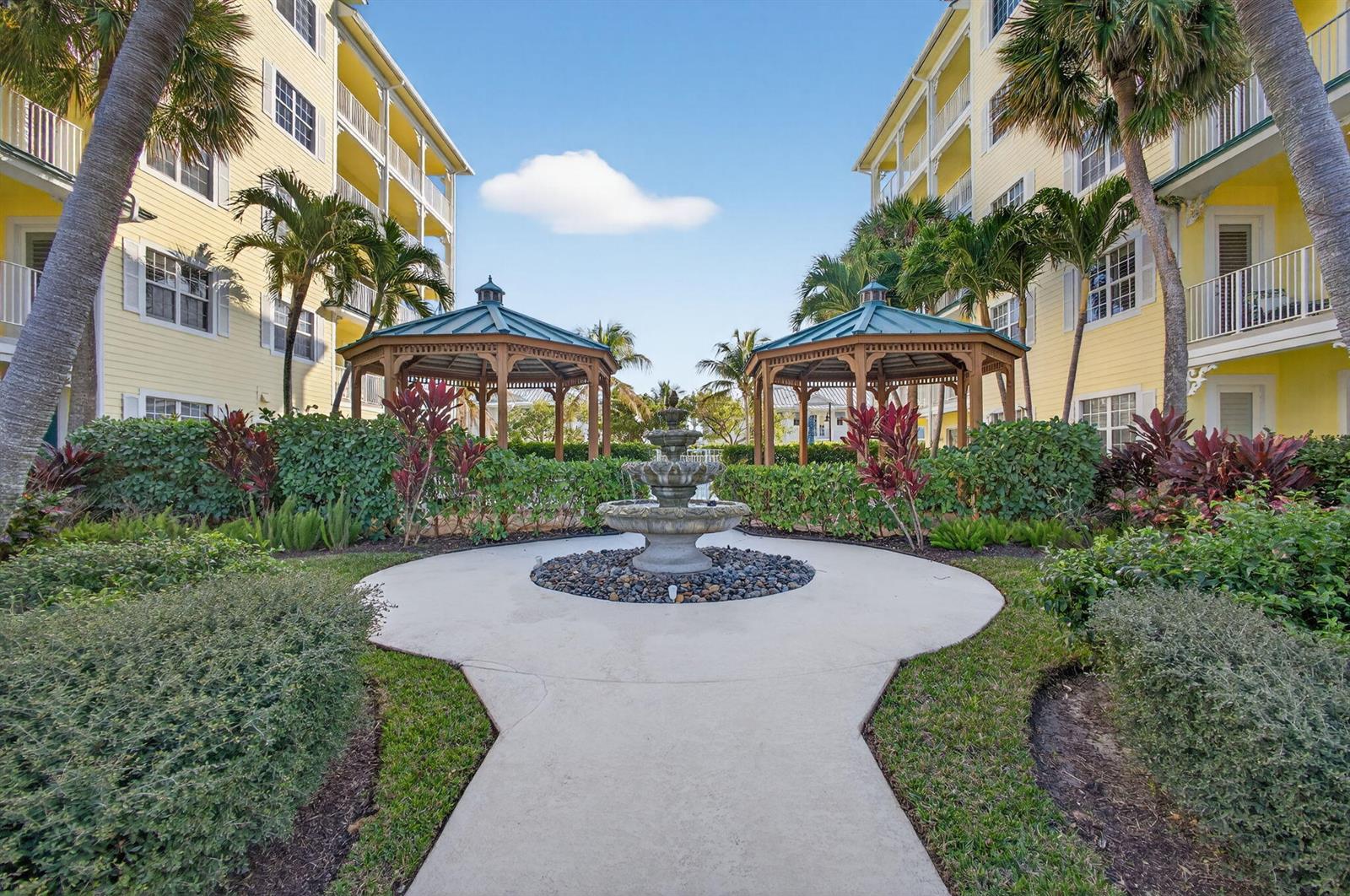 A stone fountain sits on a concrete path between two gazebos and yellow apartment buildings — 800 Juno Ocean Walk # 304, Juno Beach FL 33408, JUNO BEACH, FL