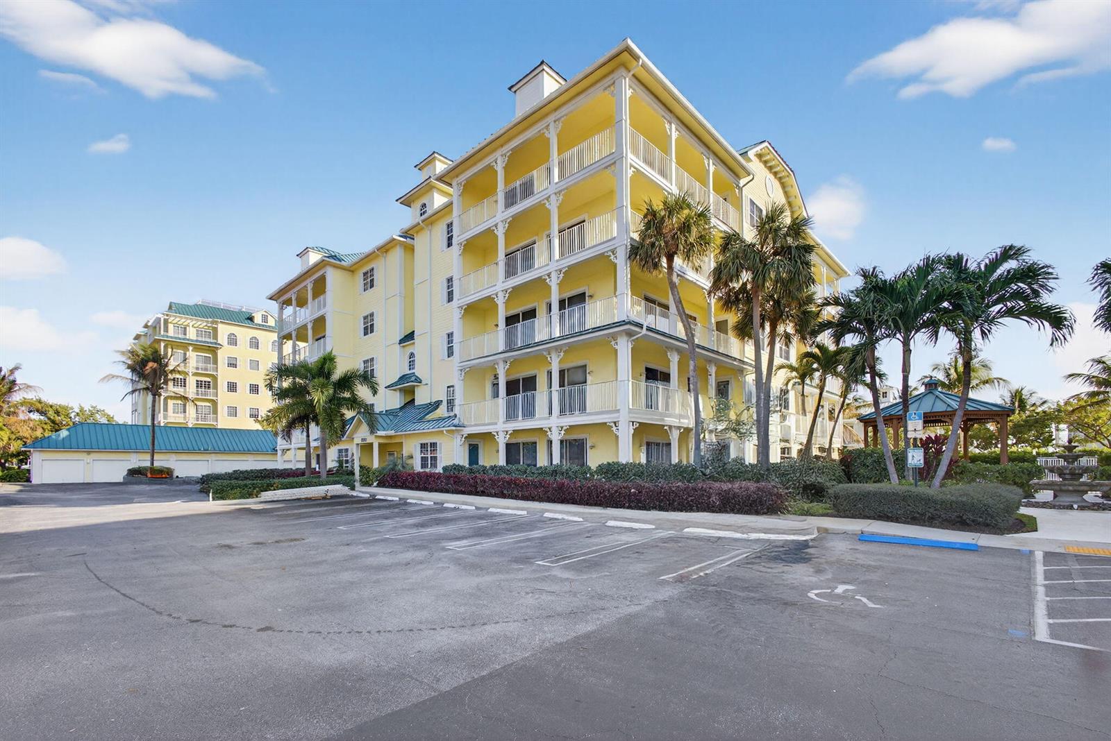 A multi-story yellow apartment building with balconies stands next to a parking lot — 800 Juno Ocean Walk # 304, Juno Beach FL 33408, JUNO BEACH, FL