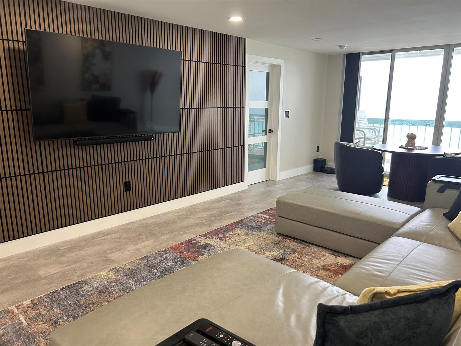 A living room features a slatted wood accent wall, a large television, and a sectional sofa — 9940 S Ocean Drive # 802, Jensen Beach FL 34957, JENSEN BEACH, FL