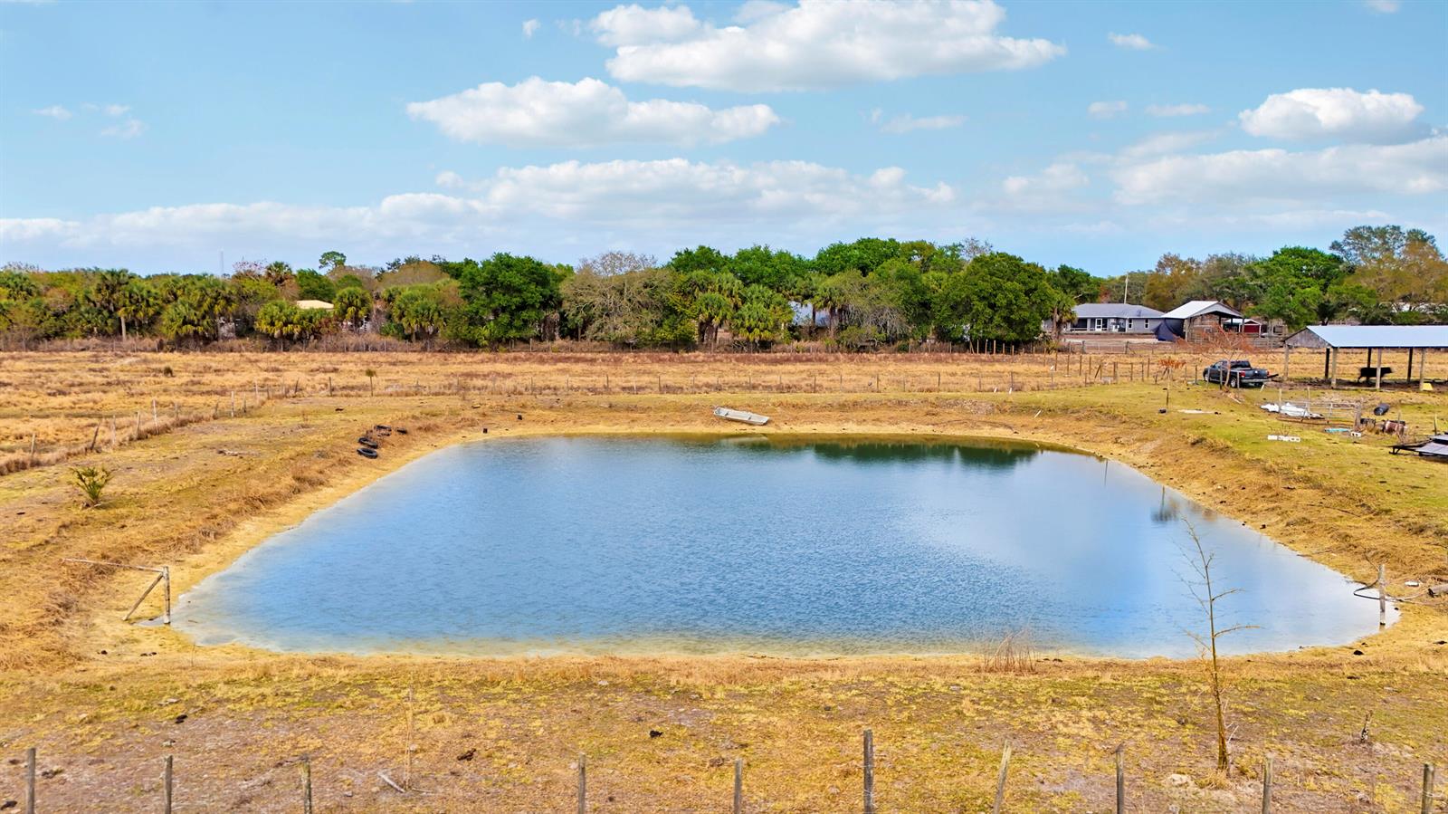 A rectangular pond sits in the center of a dry, grassy field under a blue sky — Tbd S Brocksmith Road, Fort Pierce FL 34945, FORT PIERCE, FL