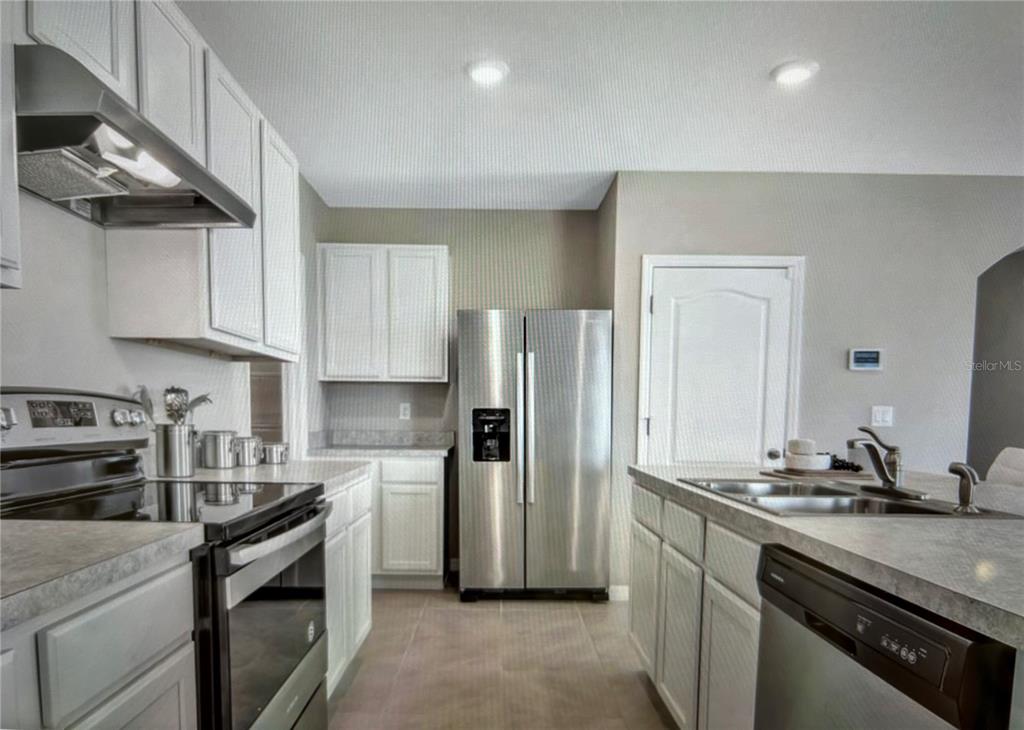 A kitchen features white cabinets, stainless steel appliances, a center island, and tiled flooring — 3464 SANDALWOOD ISLE WAY, OCOEE, FL