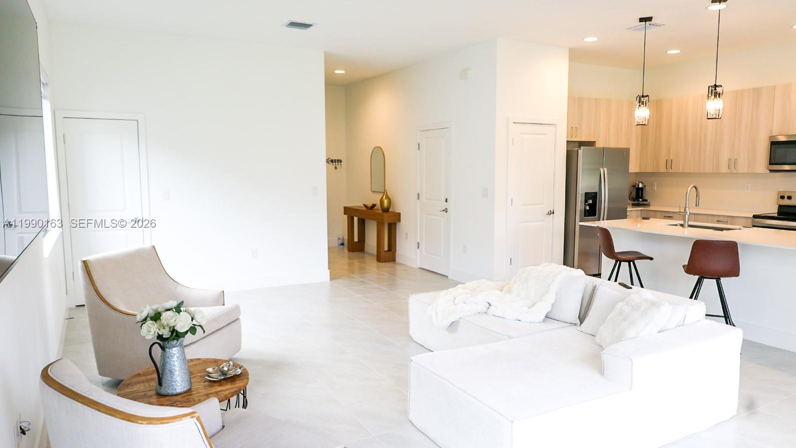An open-concept living area features a white sofa, two armchairs, and a modern kitchen — 5868 Agostino Way, Ave Maria FL 34142, AVE MARIA, FL