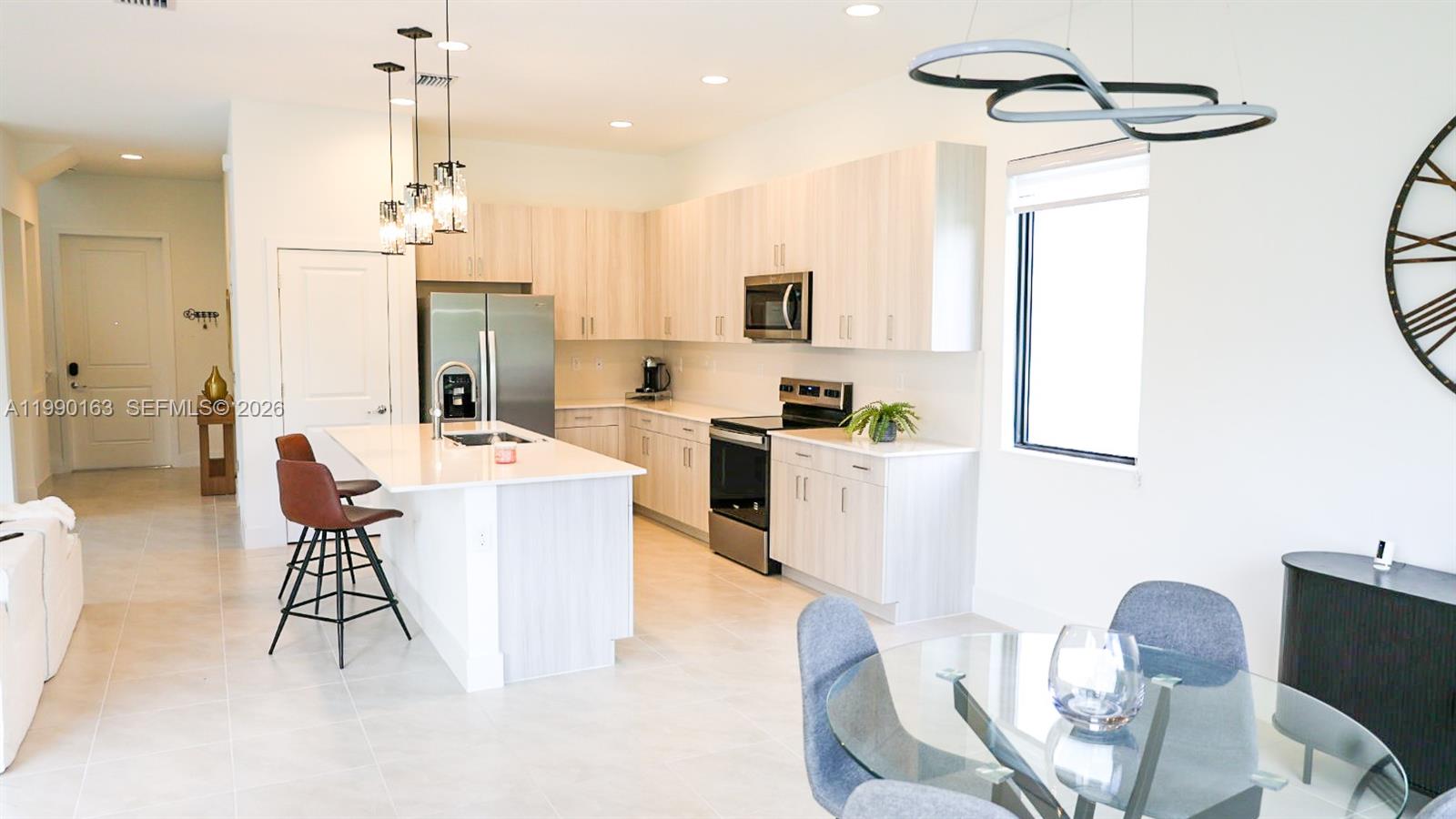 A modern kitchen features light wood cabinets, stainless steel appliances, and a central island — 5868 Agostino Way, Ave Maria FL 34142, AVE MARIA, FL