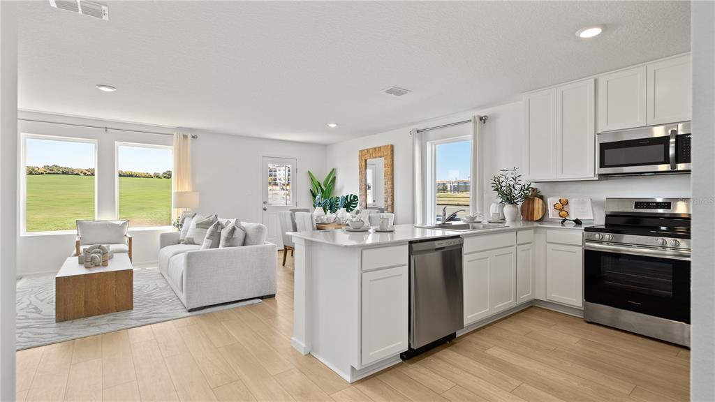An open-concept kitchen and living area features white cabinetry, stainless steel appliances, and light flooring — 3334 WANDEL TERRACE, DAVENPORT, FL